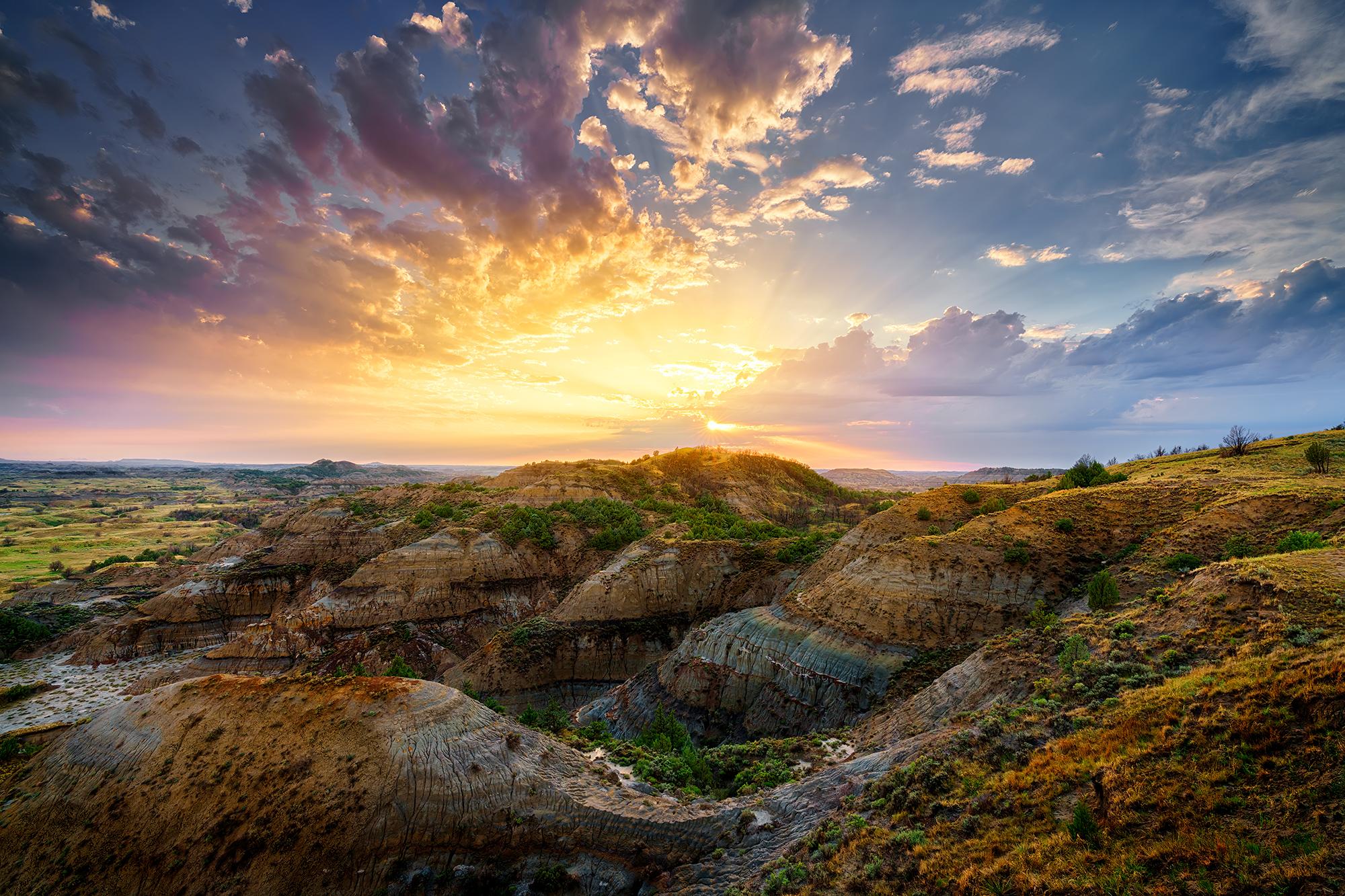 The setting sun shines through the remaining clouds from a summer thunderstorm in the badlands of North Dakota at Theodore Roosevelt National Park.